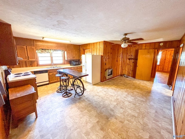 kitchen with wooden walls, white appliances, a textured ceiling, light tile patterned floors, and ceiling fan