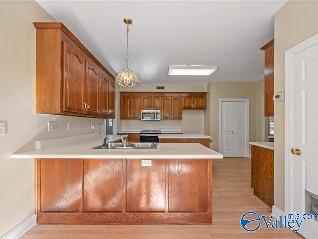 kitchen with kitchen peninsula, light wood-type flooring, stainless steel appliances, sink, and hanging light fixtures