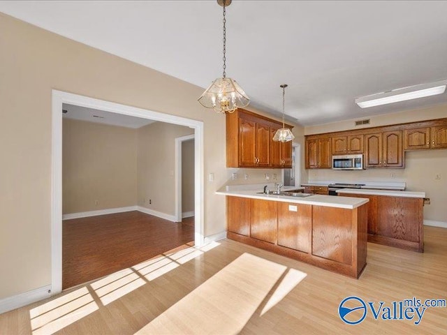 kitchen with decorative light fixtures, light wood-type flooring, sink, and appliances with stainless steel finishes