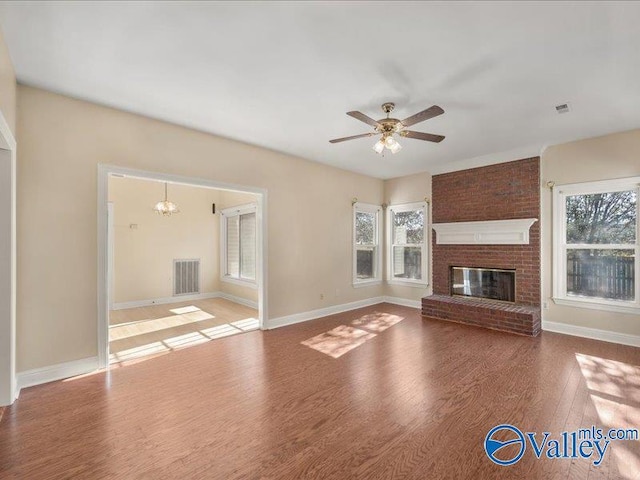 unfurnished living room featuring wood-type flooring, ceiling fan with notable chandelier, and a brick fireplace