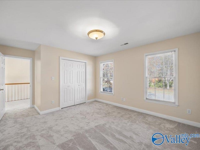 unfurnished bedroom with a closet, multiple windows, and light colored carpet