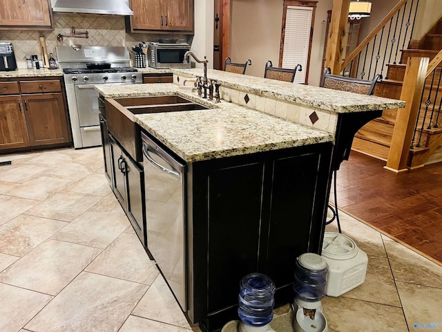 kitchen with backsplash, light tile patterned floors, stainless steel appliances, wall chimney exhaust hood, and a sink