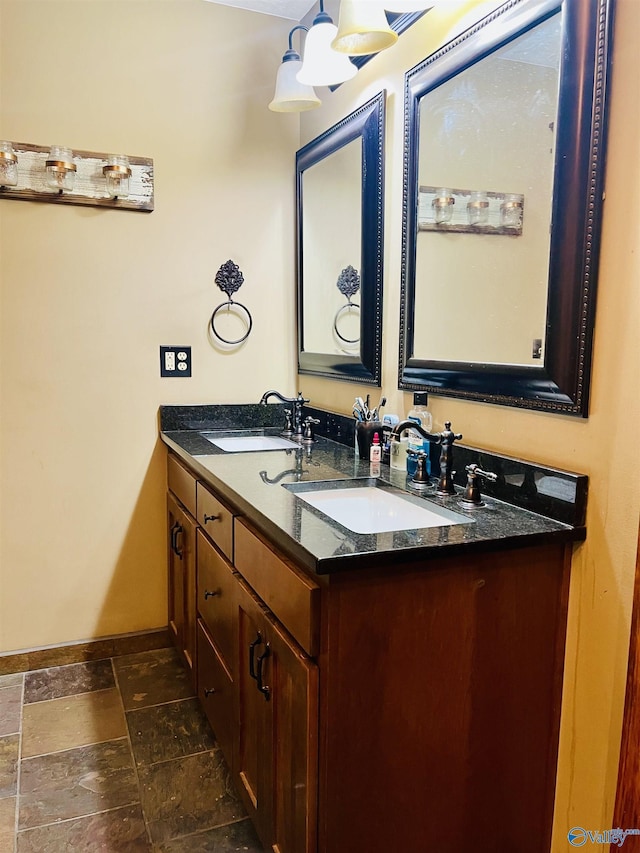 full bath featuring a sink, baseboards, stone tile floors, and double vanity