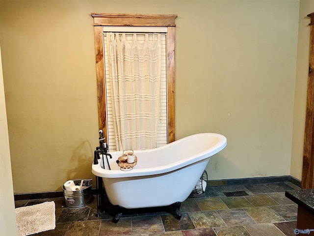 bathroom featuring a soaking tub, stone tile floors, and baseboards