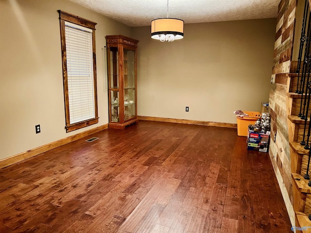 unfurnished dining area featuring hardwood / wood-style floors, baseboards, visible vents, and a textured ceiling