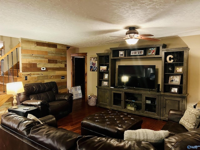 living room featuring stairway, wooden walls, wood finished floors, ceiling fan, and a textured ceiling