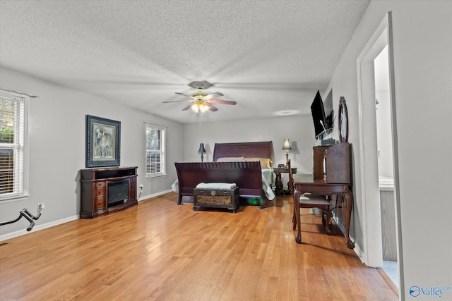 bedroom featuring ceiling fan, a fireplace, light hardwood / wood-style floors, and a textured ceiling