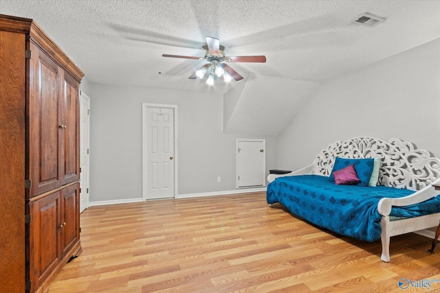 bedroom featuring ceiling fan, vaulted ceiling, a textured ceiling, and light hardwood / wood-style flooring