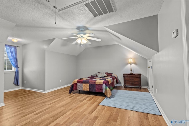 bedroom with ceiling fan, vaulted ceiling, light hardwood / wood-style floors, and a textured ceiling