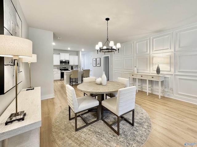 dining space with a decorative wall, recessed lighting, light wood-type flooring, and an inviting chandelier