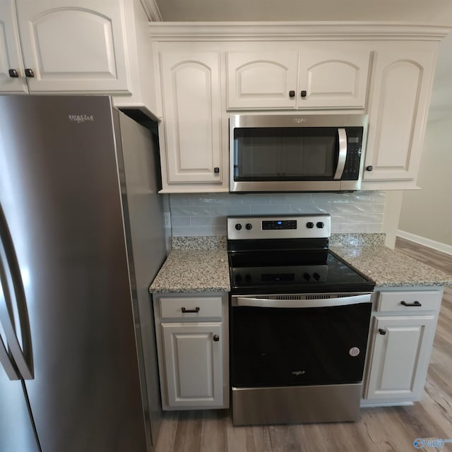 kitchen featuring appliances with stainless steel finishes, white cabinetry, light stone counters, and light hardwood / wood-style floors