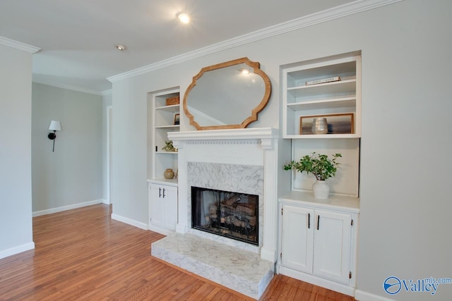 unfurnished living room featuring wood finished floors, a high end fireplace, baseboards, built in features, and crown molding