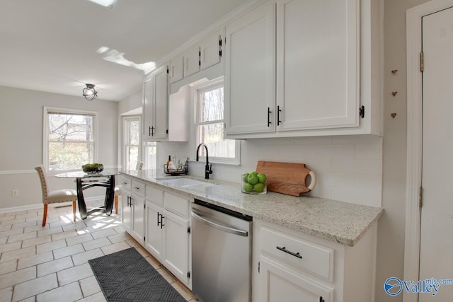 kitchen featuring tasteful backsplash, white cabinets, light stone counters, stainless steel dishwasher, and a sink