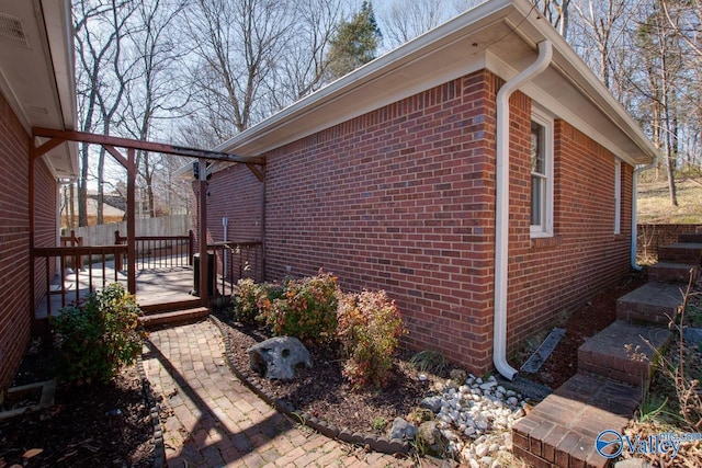 view of property exterior with brick siding, fence, and a wooden deck