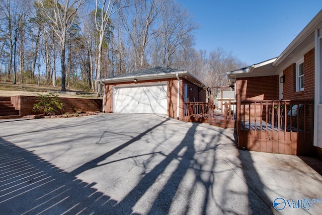 view of side of home featuring a garage, a deck, aphalt driveway, and brick siding