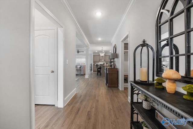 corridor featuring crown molding, light hardwood / wood-style flooring, and an inviting chandelier