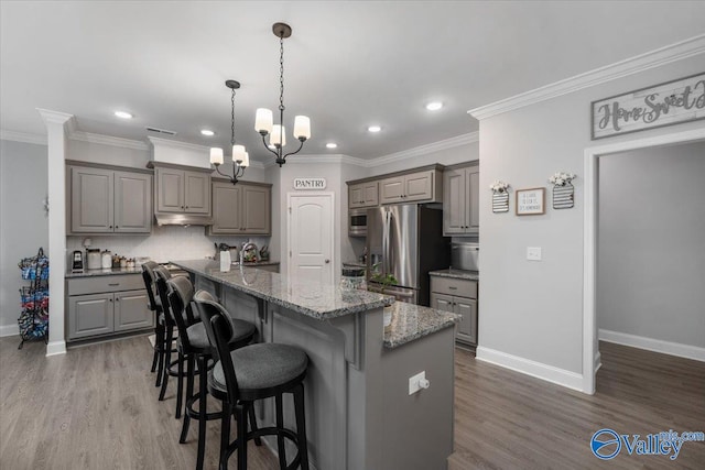 kitchen featuring dark stone counters, stainless steel appliances, hardwood / wood-style flooring, a kitchen island, and hanging light fixtures