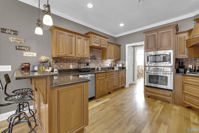 kitchen with dark stone counters, stainless steel appliances, a breakfast bar area, and light wood-type flooring