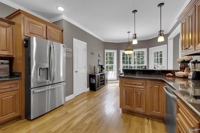 kitchen featuring dark stone countertops, crown molding, light wood-type flooring, hanging light fixtures, and appliances with stainless steel finishes