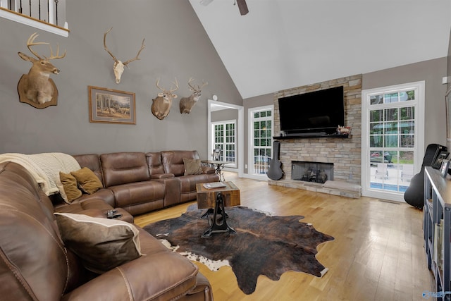 living room with ceiling fan, a fireplace, light hardwood / wood-style flooring, and high vaulted ceiling