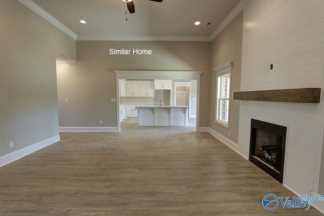 unfurnished living room featuring ornamental molding, a ceiling fan, light wood-style floors, a fireplace, and baseboards