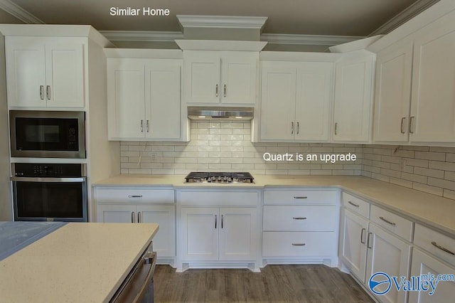 kitchen with wood finished floors, stainless steel appliances, white cabinets, under cabinet range hood, and crown molding