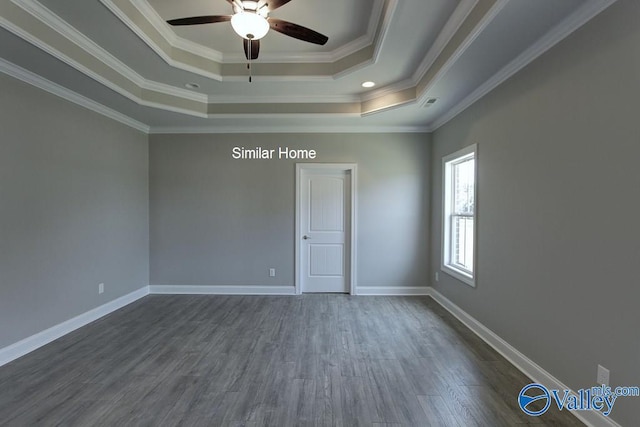 empty room with dark wood-type flooring, a ceiling fan, a tray ceiling, crown molding, and baseboards