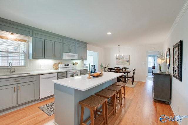 kitchen with a kitchen breakfast bar, light wood-type flooring, a sink, a chandelier, and white appliances