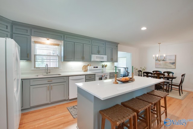kitchen with a sink, white appliances, light wood-type flooring, a kitchen bar, and backsplash