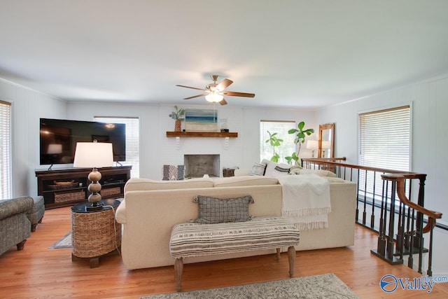 living room with light wood-style floors, ornamental molding, a fireplace, and ceiling fan