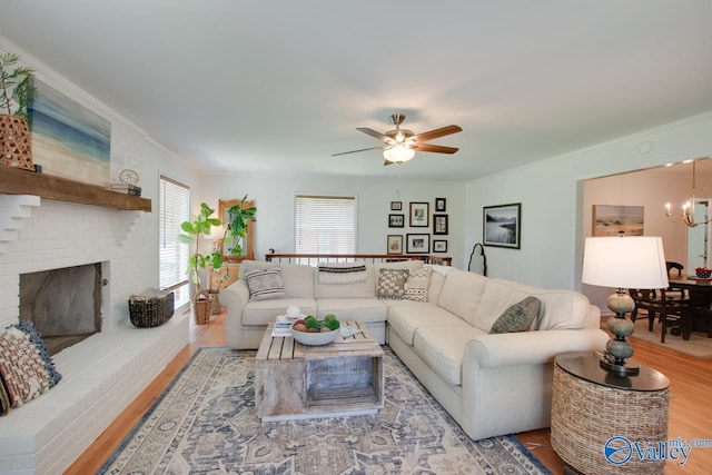 living room featuring crown molding, a brick fireplace, ceiling fan with notable chandelier, and wood finished floors