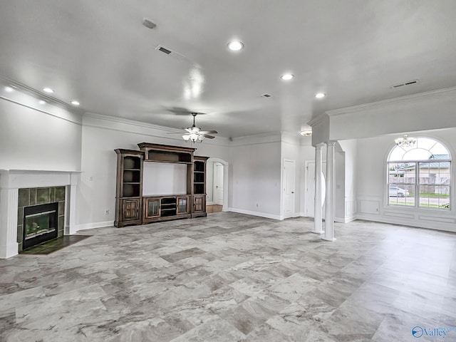 unfurnished living room featuring ceiling fan, crown molding, ornate columns, and a tiled fireplace