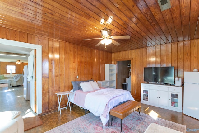 bedroom with ceiling fan, wood walls, wooden ceiling, and white refrigerator