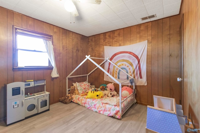 bedroom with wood walls, hardwood / wood-style floors, and ceiling fan