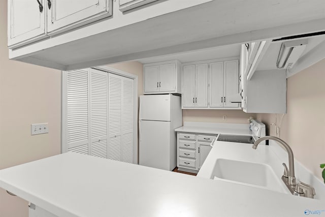 kitchen with white appliances, a peninsula, light countertops, white cabinets, and a sink