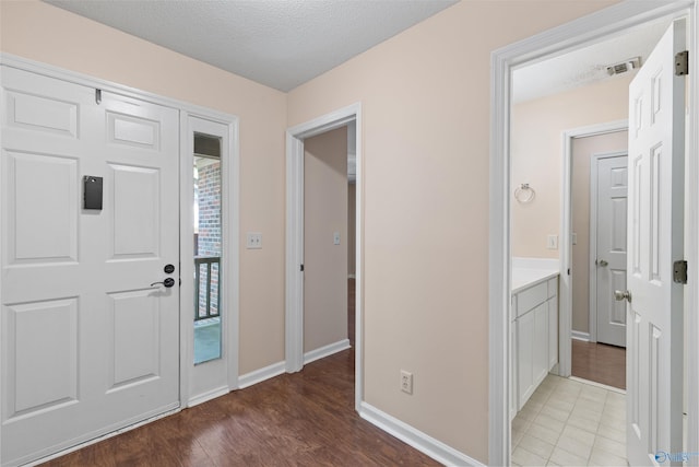 foyer entrance with light wood-style flooring, visible vents, baseboards, and a textured ceiling