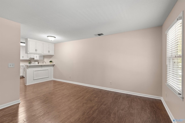unfurnished living room featuring visible vents, dark wood-style flooring, and baseboards