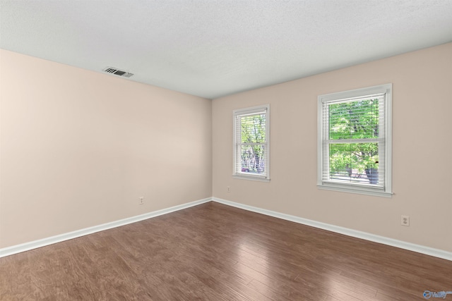 empty room featuring dark wood-style flooring, baseboards, and visible vents