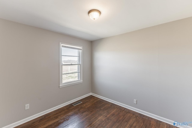 empty room featuring dark wood-type flooring, baseboards, and visible vents