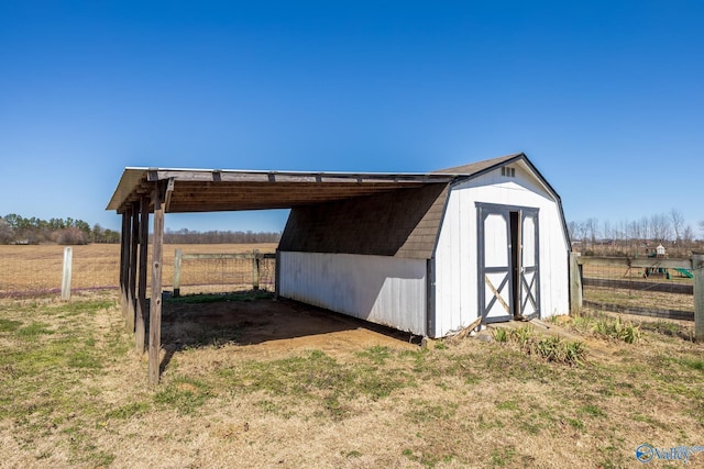 view of outbuilding featuring fence, an outbuilding, a carport, and a rural view