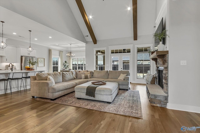 living room with french doors, beam ceiling, high vaulted ceiling, light wood-type flooring, and a fireplace