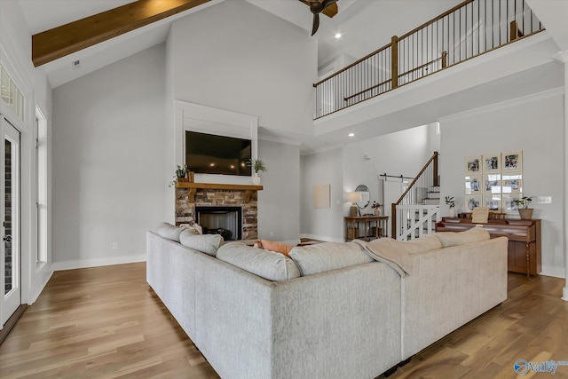 living room featuring high vaulted ceiling, a stone fireplace, light hardwood / wood-style floors, and beamed ceiling