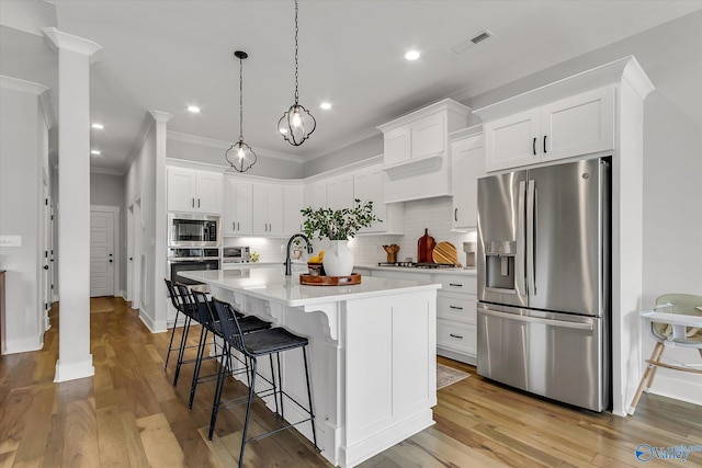 kitchen featuring pendant lighting, crown molding, white cabinetry, stainless steel appliances, and a center island with sink