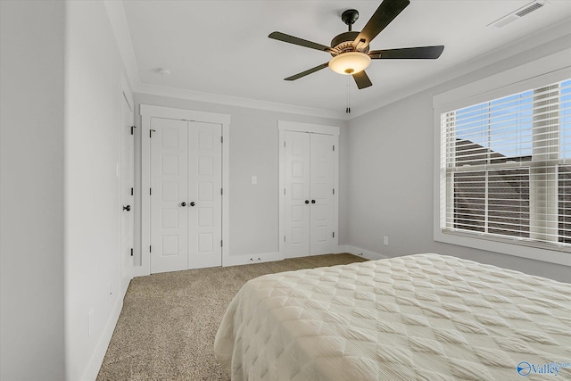 unfurnished bedroom featuring crown molding, two closets, carpet floors, and ceiling fan