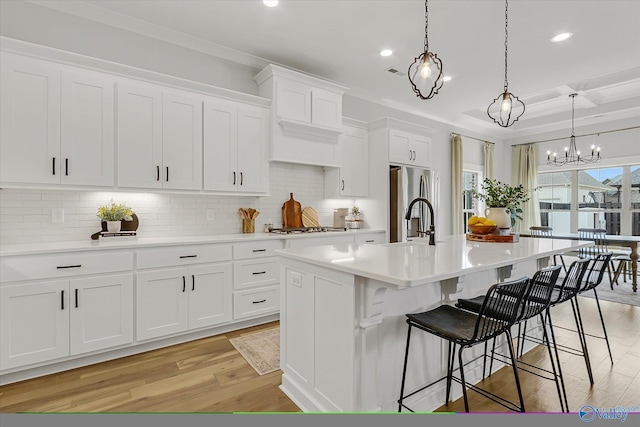 kitchen featuring pendant lighting, stainless steel fridge, a breakfast bar, a kitchen island with sink, and white cabinets