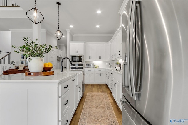 kitchen with white cabinetry, hanging light fixtures, stainless steel appliances, tasteful backsplash, and a center island with sink