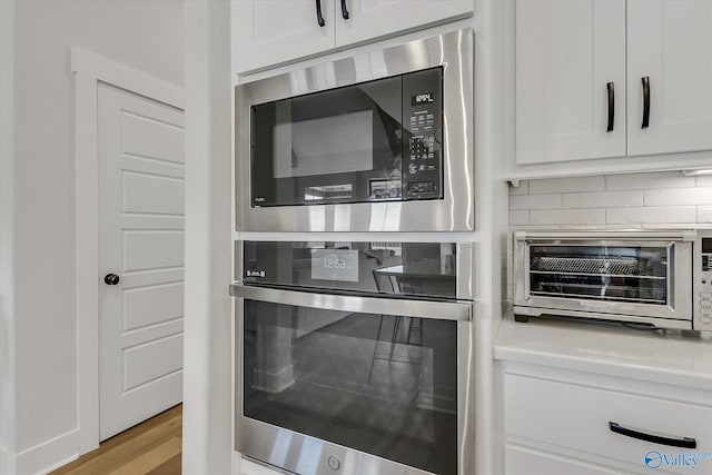 details with built in microwave, white cabinetry, decorative backsplash, and stainless steel oven