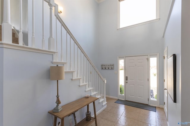 tiled entrance foyer with baseboards, a high ceiling, and stairs