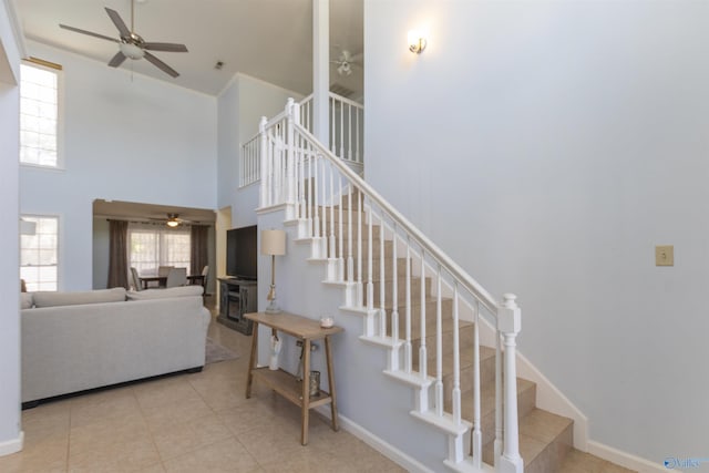 stairs featuring tile patterned floors, baseboards, a high ceiling, and a ceiling fan