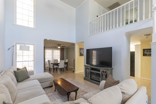 tiled living area with visible vents, crown molding, ceiling fan, baseboards, and a high ceiling